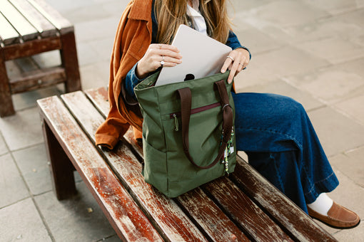 Pessoa guardando o notebook na Tote Bag Minuano verde araucária da Allcatrazes em um banco de praça