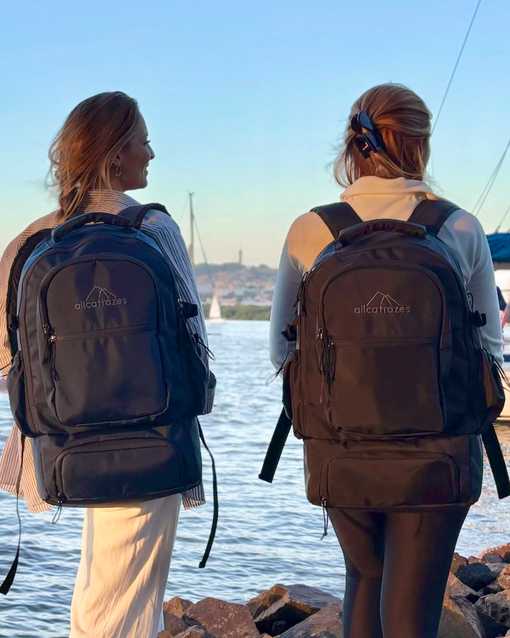 Duas pessoas caminham por um porto carregando a Mochila Alfa 3.0 preta de 33L da Allcatrazes