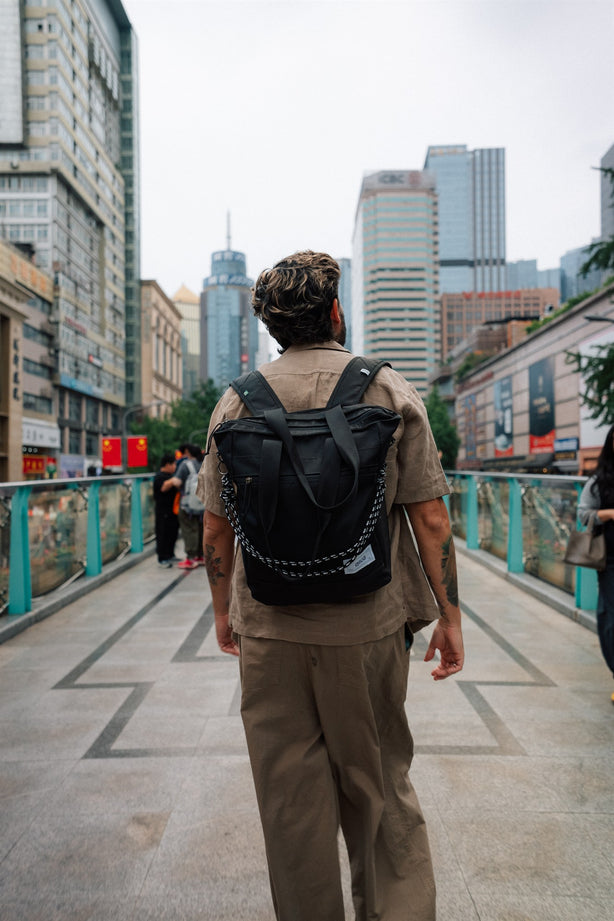 Homem de costas em passarela na China usando a bolsa tote-mochila Allcatrazes preta com corda estampada