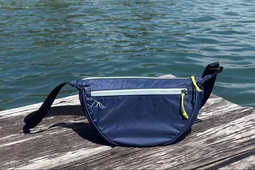 Bolsa transversal Índia Allca Allcatrazes Azul Marinho em nylon técnico hidrorrepelente, 4L - lifestyle sobre píer de madeira com mar e coqueiros ao fundo