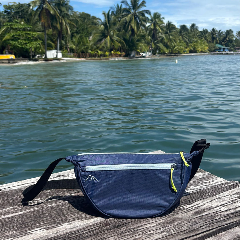 Bolsa transversal Índia Allca Allcatrazes Azul Marinho em nylon técnico hidrorrepelente, 4L - lifestyle sobre píer de madeira com mar e coqueiros ao fundo