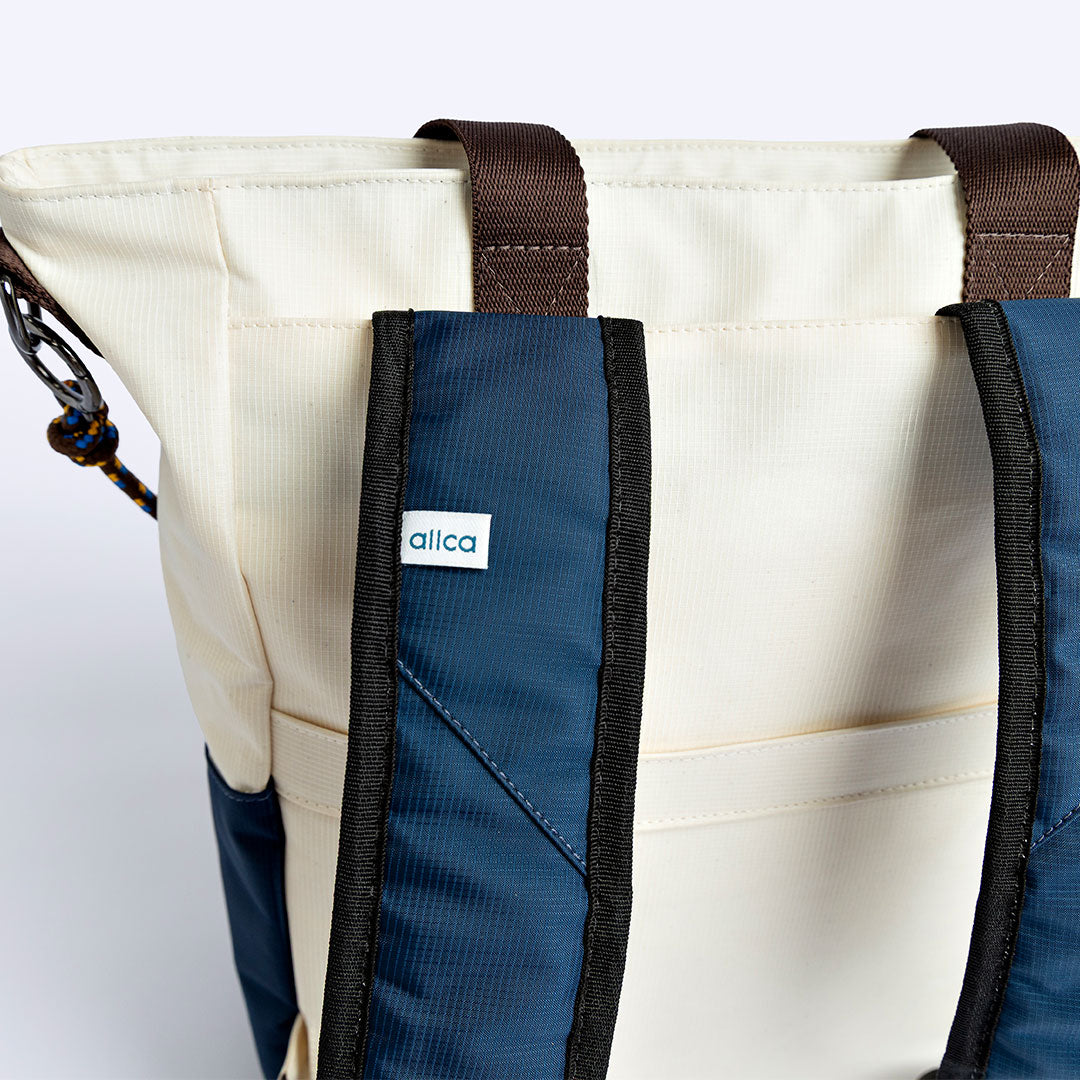 Tote Bag Allcatrazes Allca x Brasco Off White Encontro em tecido hidrorrepelente - detalhe das alças mochila azul marinho e etiqueta allca