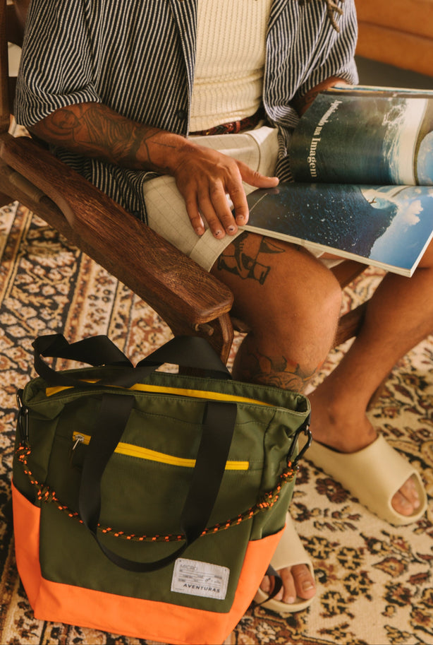 home sentado lendo revista ao lado uma tote bag verde cachoeira allcatrazes the summer hunter